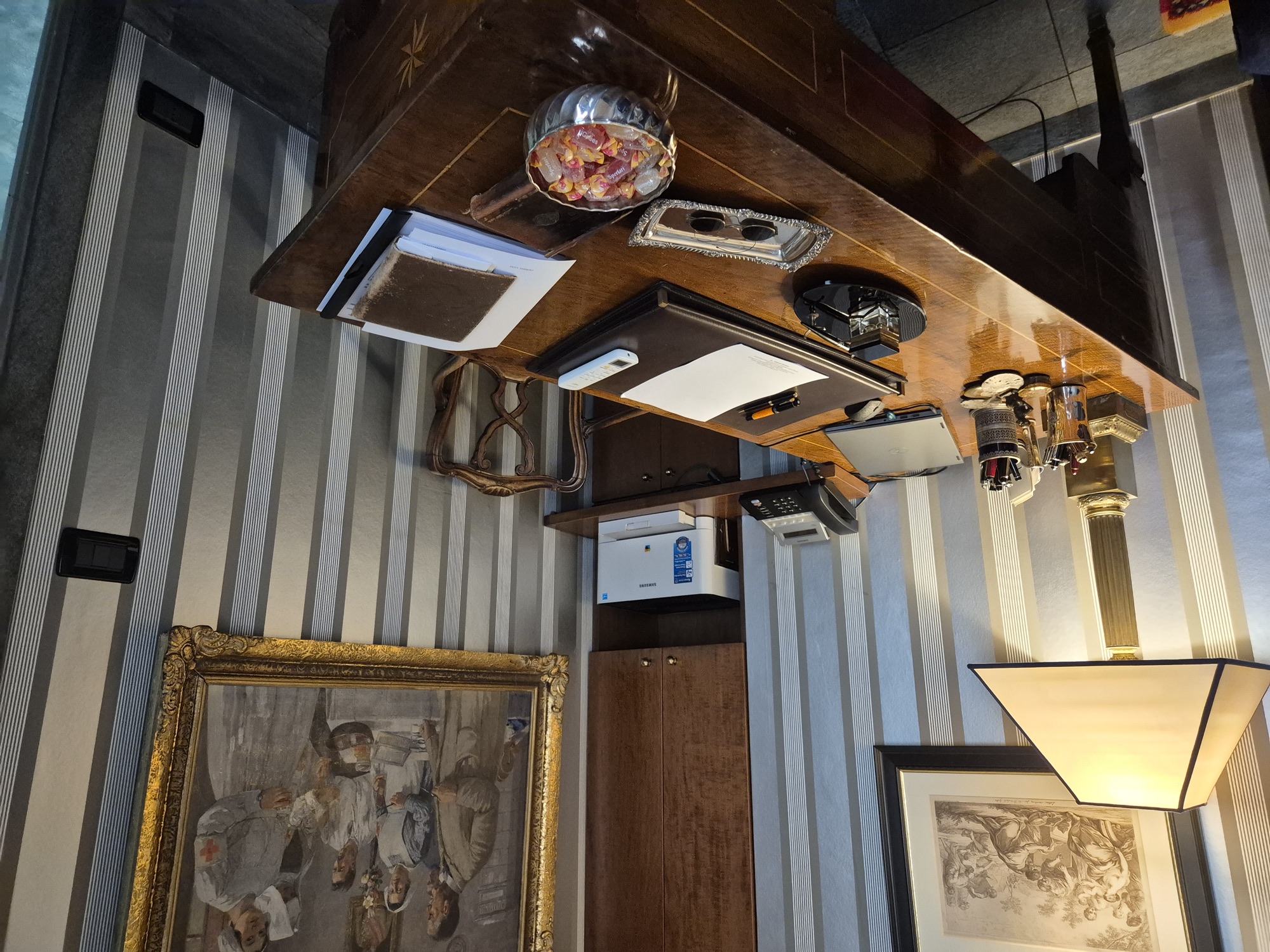 Lo studio: scrivania in legno intarsiato, lampada, un dipinto con cornice dorata e pareti a righe